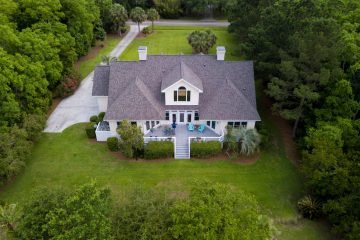 Aerial view of large home with new roof on wooded grassy property